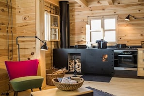 A cozy cabin interior with a wooden interior, a black stove, a red chair, and a kitchen area. - Hollmann am Berg - Toni (Ebene Reichenau)