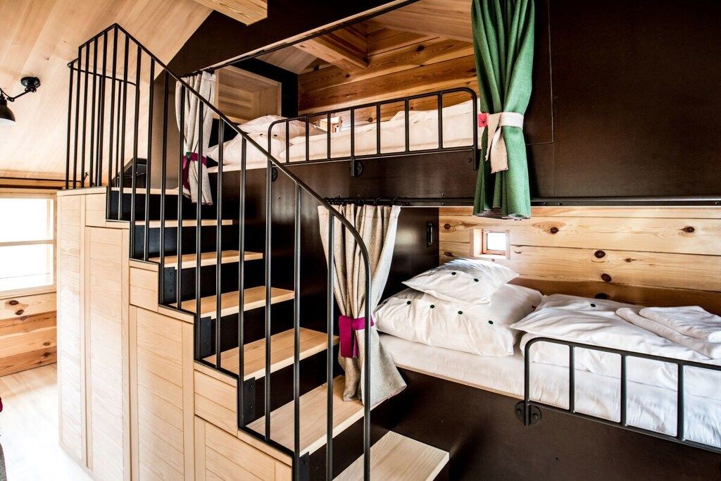 Habitació amb literes, escala de fusta i cortina.