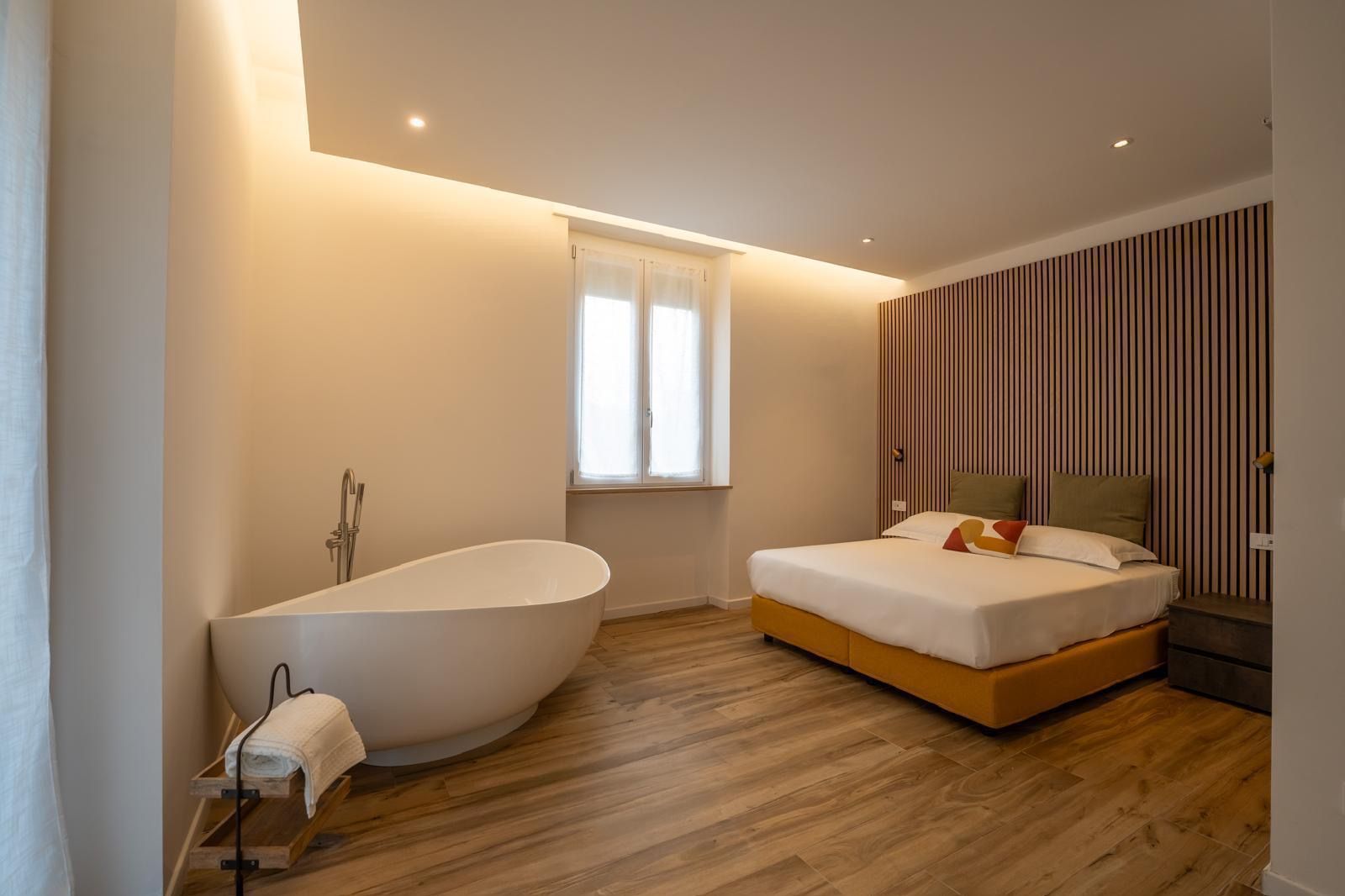 Une chambre moderne avec une baignoire sur pieds, un lit agrémenté de plusieurs coussins et une fenêtre avec des rideaux.