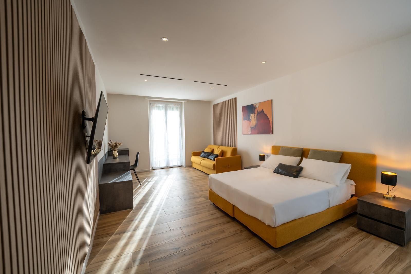 A modern hotel room with a large bed, a sofa, a desk, and a TV.