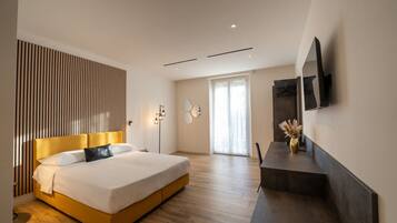 A modern bedroom with a large bed, a flat-screen TV mounted on the wall, and a sliding door leading to a balcony.