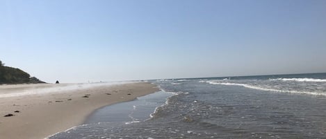 Ein Strand mit klarem Himmel, sanften Wellen und einem sandigen Ufer.