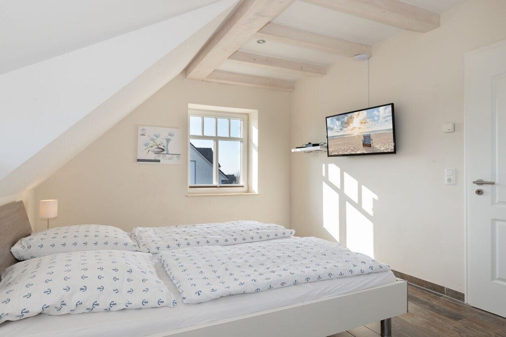 Ein Schlafzimmer mit Bett, Fenster, einem Wand-Fernseher und einer Tür.