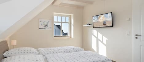 Ein Schlafzimmer mit Bett, Fenster, einem Wand-Fernseher und einer Tür.