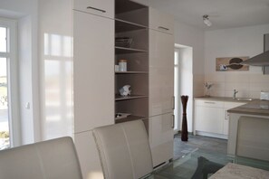 A modern kitchen with a glass dining table, white cabinets, and a view of the outdoors. - House Ostseestrand (4) (Dranske \/ OT lancken)