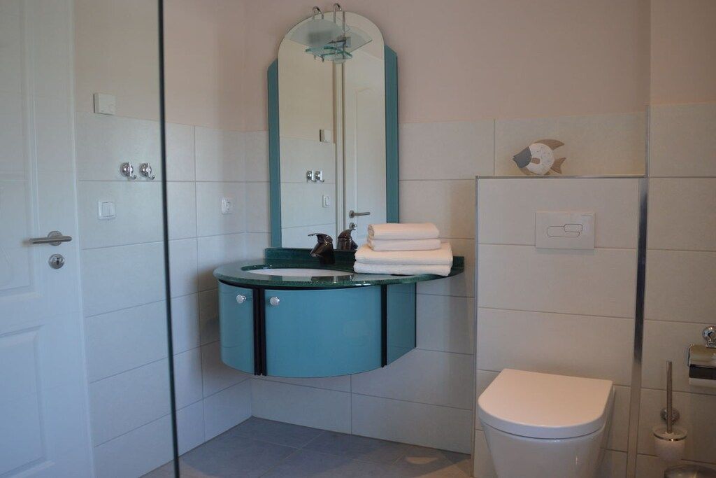 Un baño con inodoro blanco, lavamanos verde azulado y espejo superior.