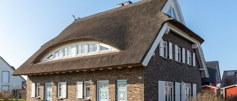 A traditional house with a steeply pitched roof, a brick facade, and a small front garden.