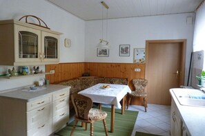 A kitchen with wooden paneling, a dining table with chairs, a cabinet with glass doors, and a hanging light fixture. - Holiday apartment with 2 bedrooms (Dessau-Roßlau)