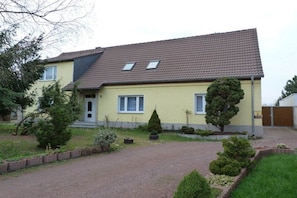 A two-story house with a sloped roof, a front porch, and a driveway leading to the entrance. - Holiday apartment with 2 bedrooms (Dessau-Roßlau)