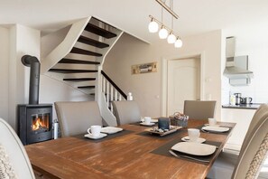 Ein Essbereich mit einem Holztisch, gedeckt für vier Personen, einem eingebauten Holzofen und einer Wendeltreppe.