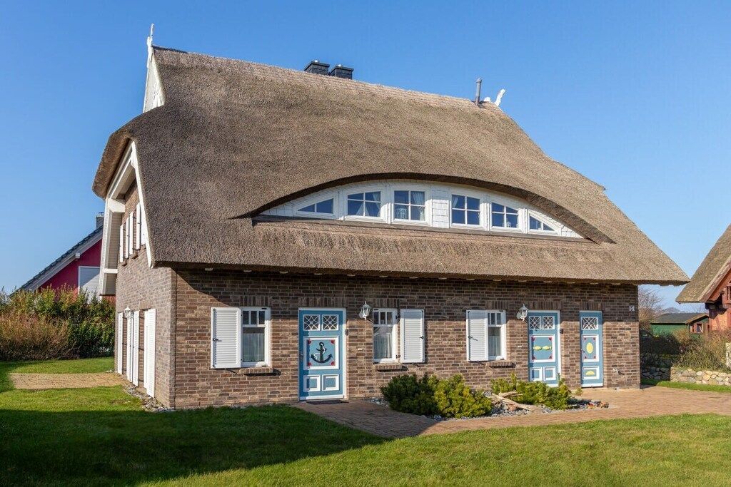 Ein Haus mit einem Strohdach, Backsteinmauern und einem kleinen Vorgarten.