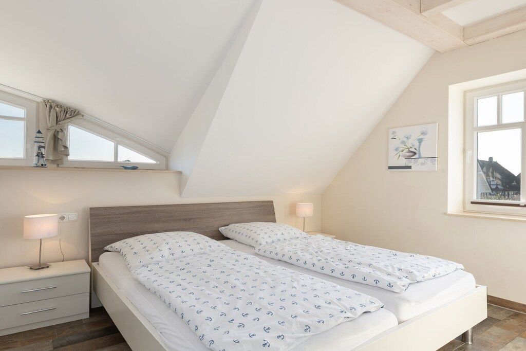 Une chambre avec un plafond en pente, deux lits avec la même literie, une table de chevet avec une lampe et une fenêtre donnant sur un beau paysage.