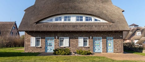 Ein traditionelles Haus mit einem Reetdach, zahlreichen Fenstern und Türen mit dekorativen Mustern.