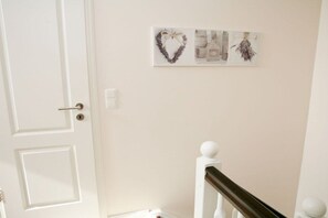 Eine weiße Tür mit runder Klinke, eine weiße Wand mit einem gerahmten Kunstwerk und eine weiße Treppe mit einer Holzhandläufe.