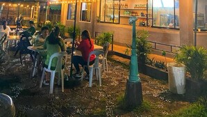 Uma área de refeições ao ar livre com mesas e cadeiras, um espaço coberto para sentar e um edifício com janelas e balcão.