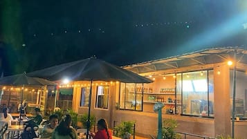 An outdoor dining area with tables and chairs, a covered seating area, and a building with windows and a counter.