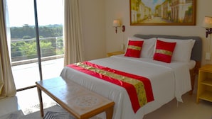 Quarto de hotel com cama, um banco, uma pintura e vista para área verde.
