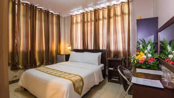 A hotel room with a bed, a desk, a chair, a lamp, and curtains.