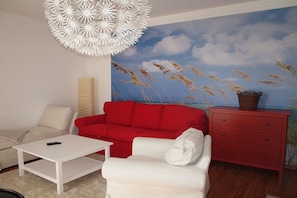 A living room with a red sofa, white armchair, and a white coffee table. There is a red dresser with a basket on top. - Karlshagen at the harbor (Karlshagen Usedom)