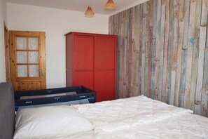 Un dormitorio con una cama, un armario, una maleta y una puerta con paneles de vidrio esmerilado.