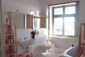 A bathroom with a white sink, mirror, and toilet, wooden shelves, and a window with blinds. - Karlshagen at the harbor (Karlshagen Usedom)