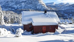 A snow-covered cabin with a red door, surrounded by snow-laden trees and mountains in the background. - Amazing home in Tjørhom with sauna (Tjørhom)
