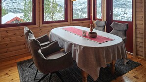 A cozy dining area with a table set for two, surrounded by wooden walls and large windows offering a view of snow-covered mountains. - Amazing home in Tjørhom with sauna (Tjørhom)