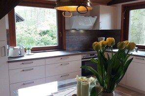 A kitchen with white cabinets, a microwave, and a window with a view of greenery. - Holiday home with 2 bedrooms (Grünheide)