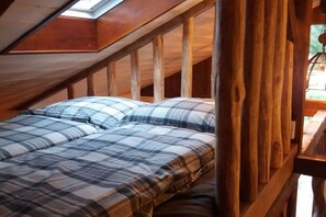 A bedroom with a sloped ceiling and wooden beams, featuring a bed with plaid bedding. - Holiday home with 2 bedrooms (Grünheide)