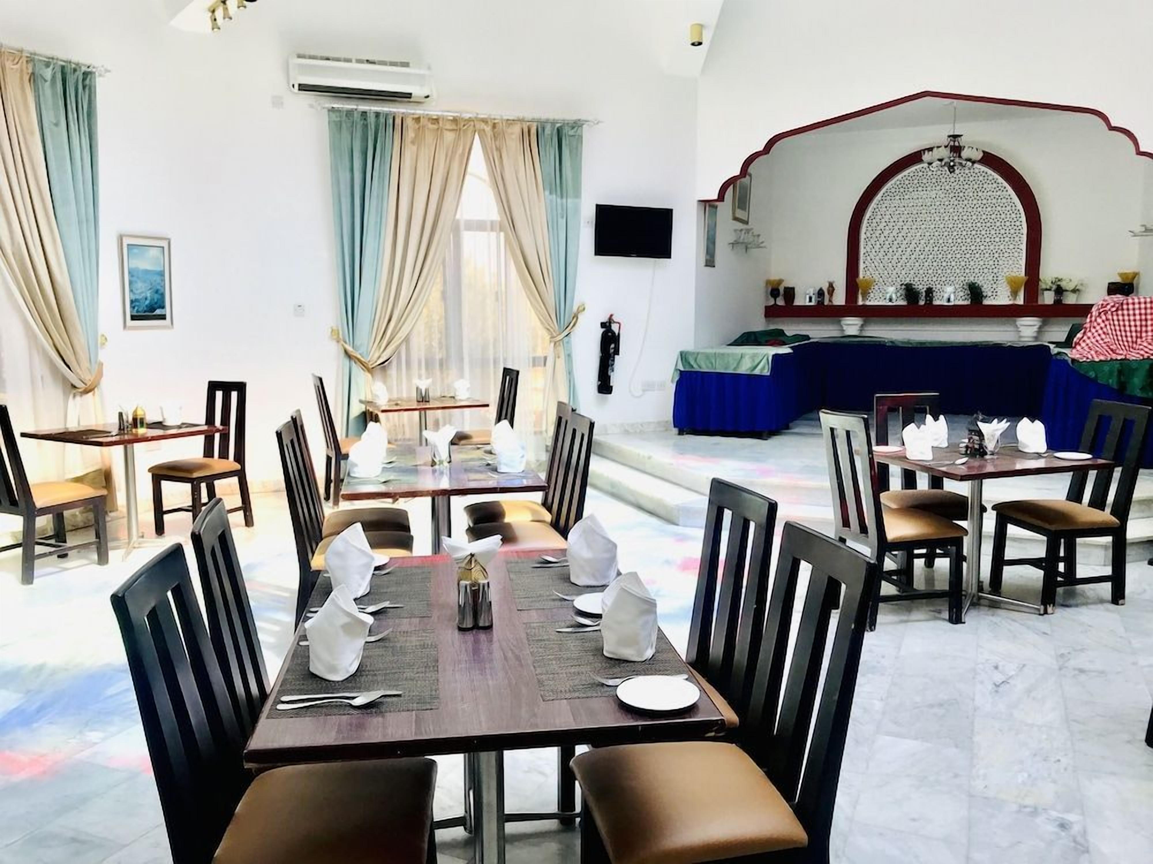 Un comedor con mesas dispuestas para cuatro, sillas y un amplio ventanal con cortinas.