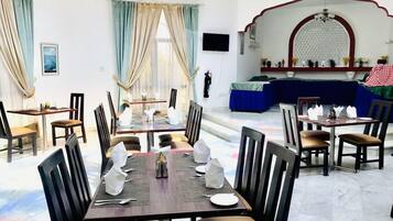 Un comedor con mesas dispuestas para cuatro, sillas y un amplio ventanal con cortinas.