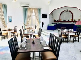 Un comedor con mesas dispuestas para cuatro, sillas y un amplio ventanal con cortinas.