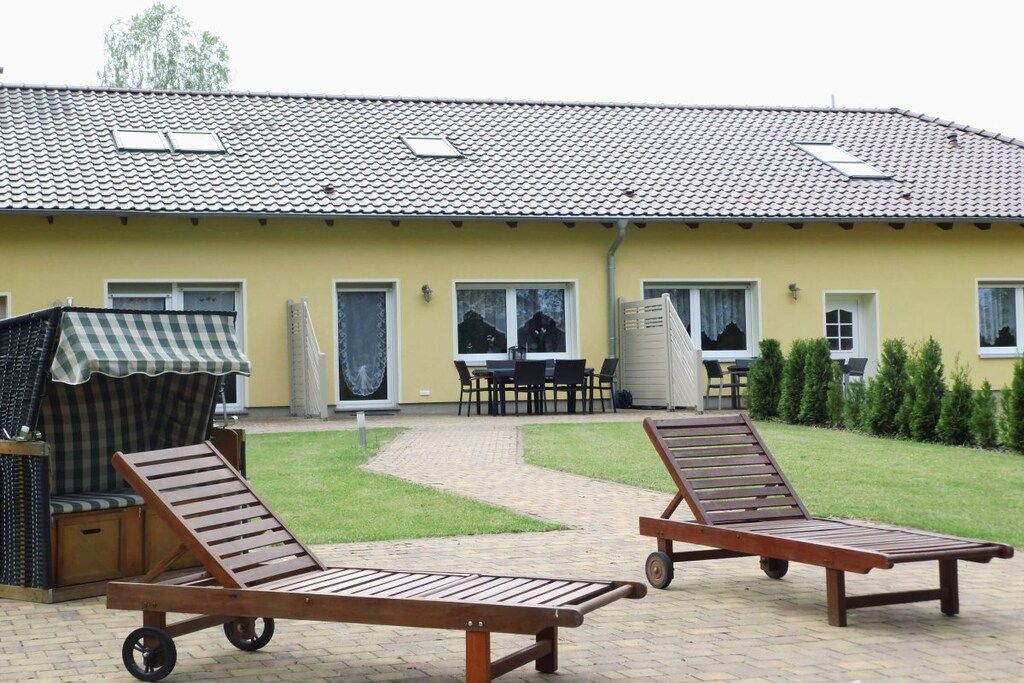 A yellow building with a tiled roof, two lounge chairs with wheels, a covered seating area, and a paved patio.
