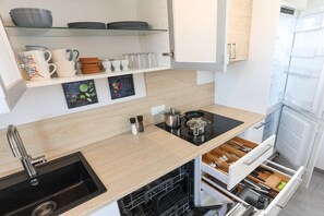 Una cocina con un lavamanos negro, encimera de madera y estufa integrada. Hay estantes sobre la encimera con vajilla y una pizarra con escritura.