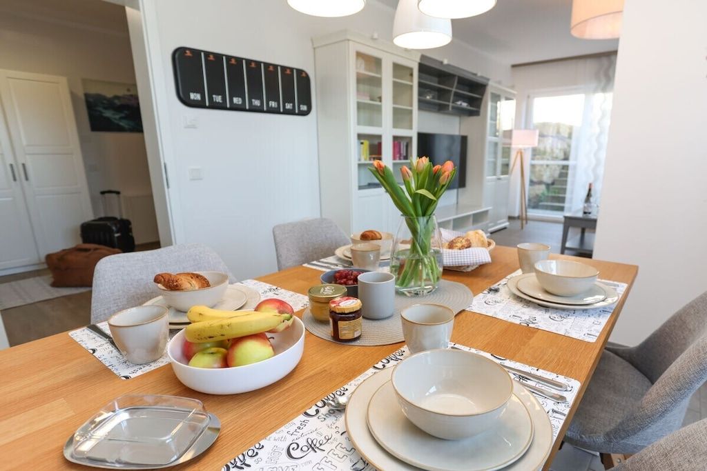 Un coin repas avec une table en bois mise pour le petit-déjeuner, comprenant des fruits, du pain et du café.
