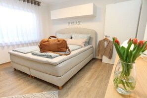 A bedroom with a bed, a brown bag, a coat hanger with a coat, and a vase with flowers. - Bad Kösen Wine Quarter (Naumburg)