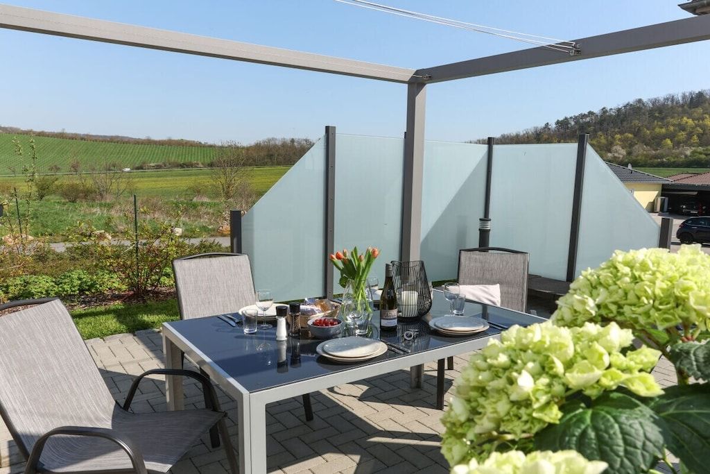 Eine Terrasse im Freien mit Esstisch und Stühlen, mit Blick auf ein grünes Feld.
