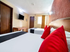 Una habitación de hotel con una cama grande, un escritorio y un televisor en la pared.