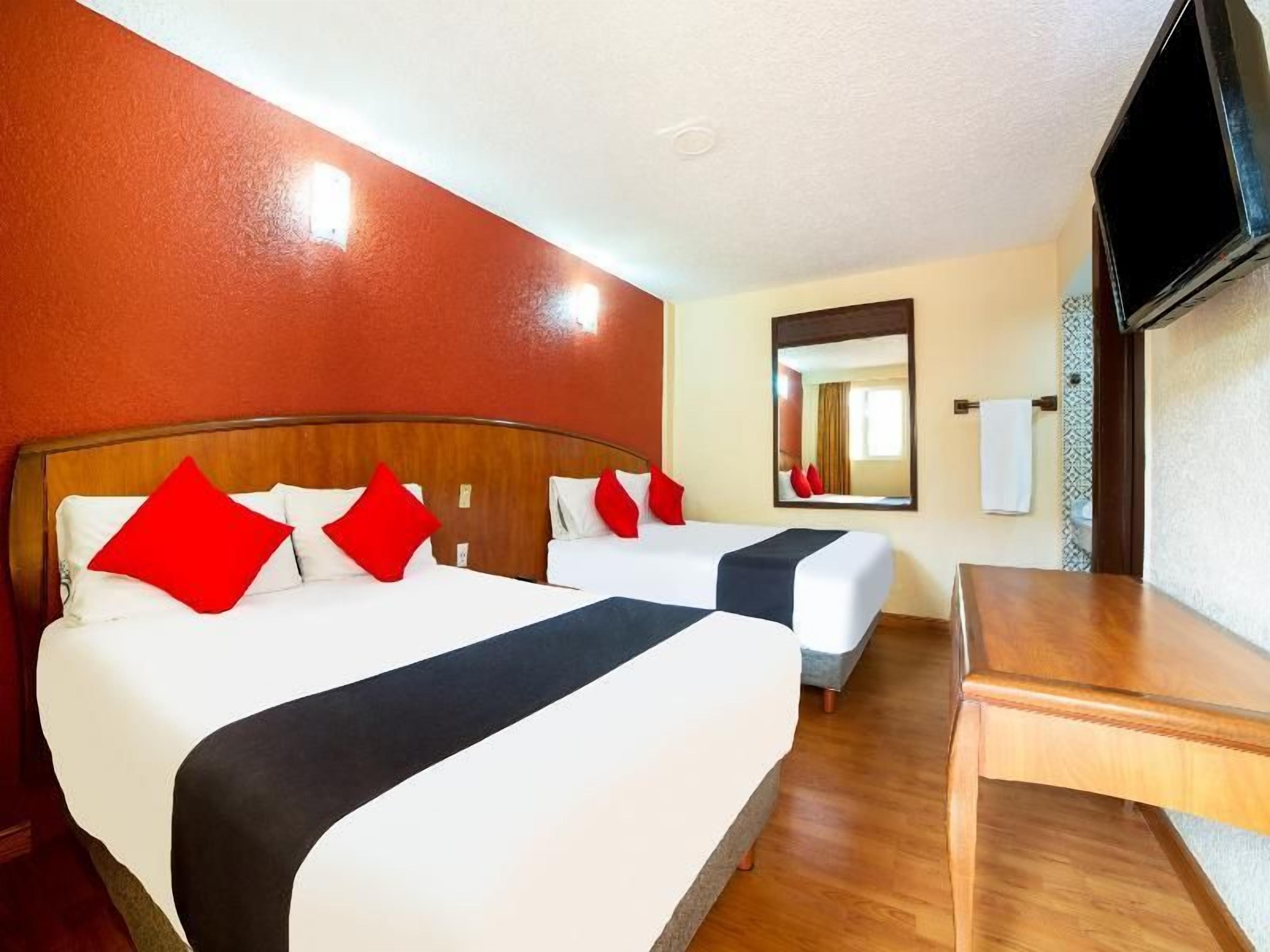Una habitación de hotel con dos camas, una mesa de madera, un televisor y un espejo.