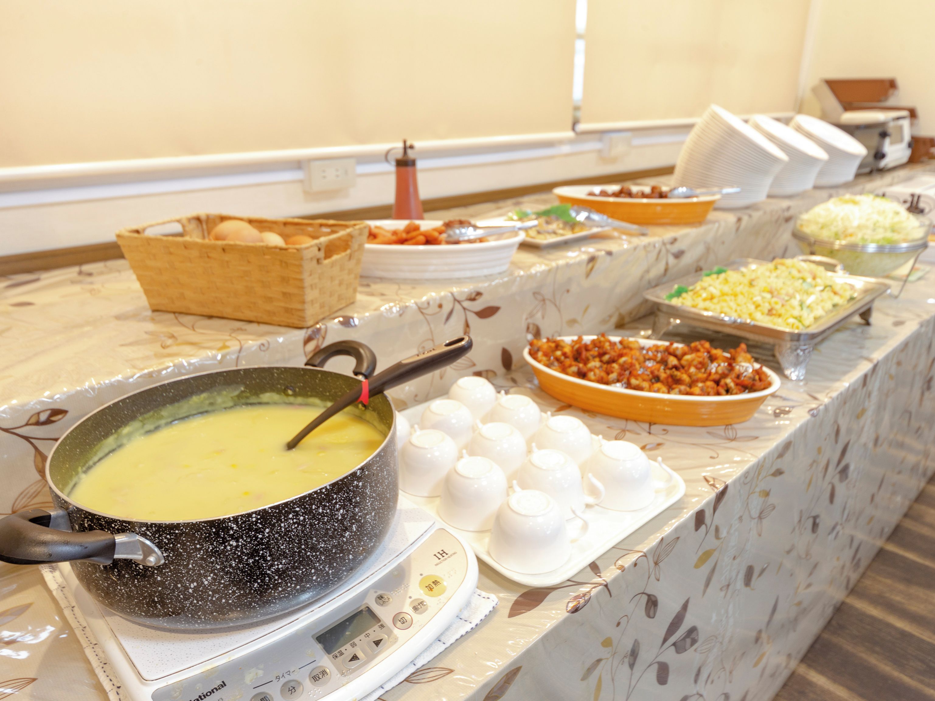 A buffet table with various food items and a pot of soup on a portable stove.