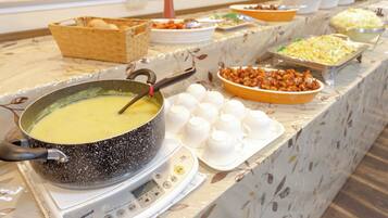A buffet table with various food items and a pot of soup on a portable stove.