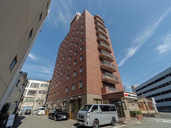 A multi-story hotel with a brick facade, a parking lot with cars, and a clear blue sky. - OYO 44047 Sun Hotel Tosu (Tosu)