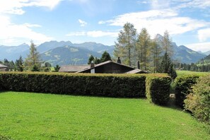 A house with a sloped roof, surrounded by a well-maintained hedge and a grassy lawn.