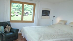 A bedroom with a bed, a chair, a window with a view, and a floor lamp.