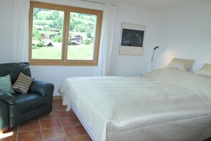 A bedroom with a bed, a chair, a window with a view, and a floor lamp.