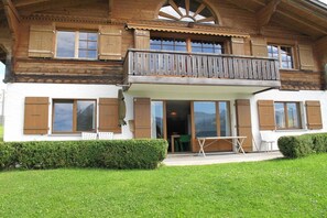 A two-story wooden house with a balcony, large windows, and a well-maintained lawn.