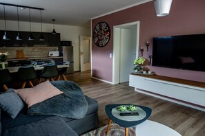 Ein modernes Wohnzimmer mit einer Couch, einem Couchtisch, einem Flachbildfernseher und einem Essbereich mit Stühlen und einem Tisch.