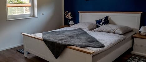 Quarto com cama, duas mesas de cabeceira, uma janela e um criado-mudo com abajur.
