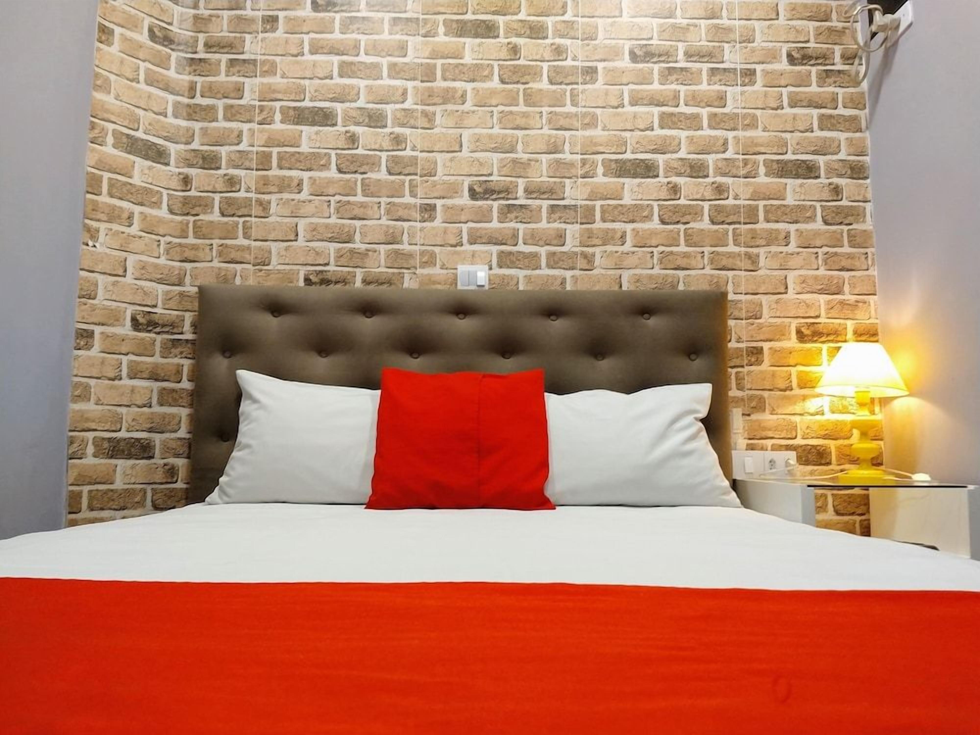 Cama com cabeceira estofada, travesseiros brancos e vermelhos, e colcha vermelha.