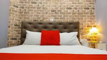 Cama com cabeceira estofada, travesseiros brancos e vermelhos, e colcha vermelha.
